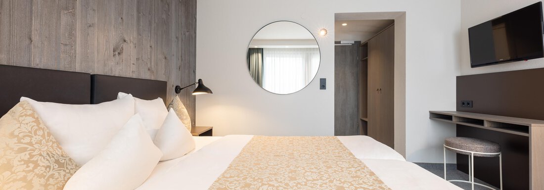 A modern bedroom with a large bed and elegant decorations. The room has light walls and a round mirror that creates a pleasant atmosphere. - Haus Verwall Appartements - Obergurgl 