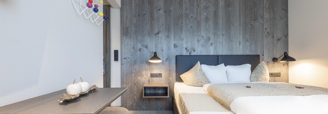 A modern hotel room with a large bed and a stylish table. The walls are painted in gray, and there are decorative elements. - Haus Verwall Appartements - Obergurgl 