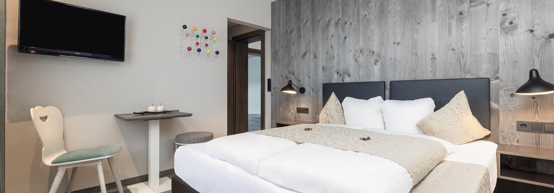 A modern room with a large bed and a cozy seating area. A television hangs on the wall and the decor is in neutral colors. - Haus Verwall Appartements - Obergurgl 