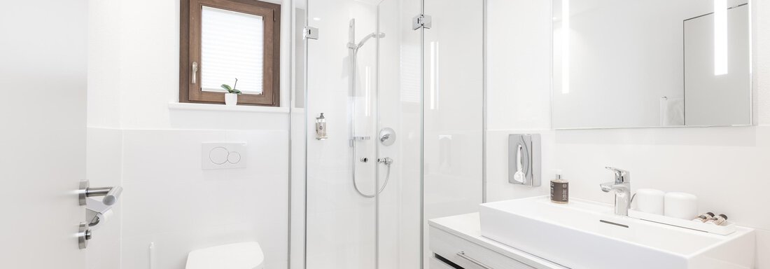 A modern bathroom with white walls and elegant furnishings. There is a shower, a sink, and a toilet, all in a light design. - Haus Verwall Appartements - Obergurgl 