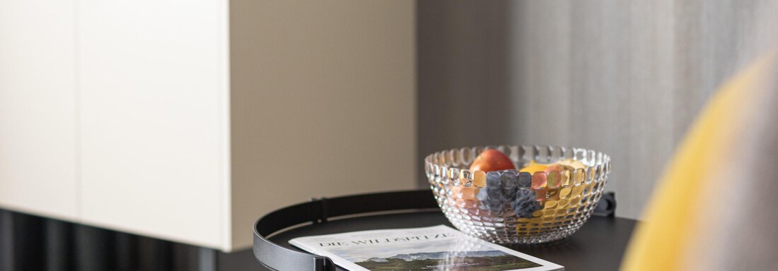 A modern side table with a glass decanter and a bowl full of fruits. In the background, there is a light-colored cabinet against the wall. - Haus Verwall Appartements - Obergurgl 