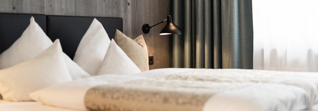 A cozy bedroom with a double bed and white bedcovers. The walls have a wood look and the curtains are green. - Haus Verwall Appartements - Obergurgl 