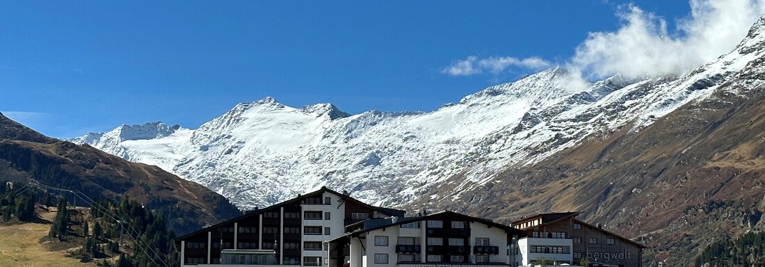 A hotel building in a picturesque mountain landscape with snow-covered peaks. The sky is blue with a few clouds. - Haus Verwall Appartements - Obergurgl 