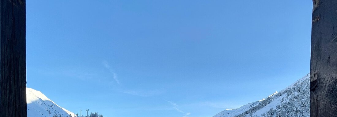 A winter mountain panorama with snow-covered hills and a clear blue sky. In the foreground, modern buildings can be seen. - Haus Verwall Appartements - Obergurgl 