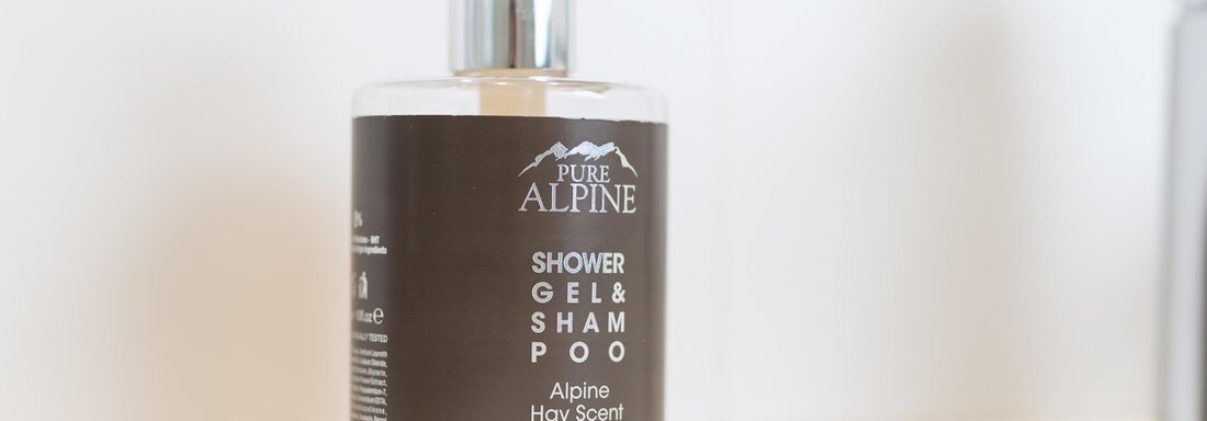 A bottle of shower gel and shampoo on a light shelf. The packaging is dark with white lettering and displays the name "Alpine Holy Scent". - Haus Verwall Appartements - Obergurgl 
