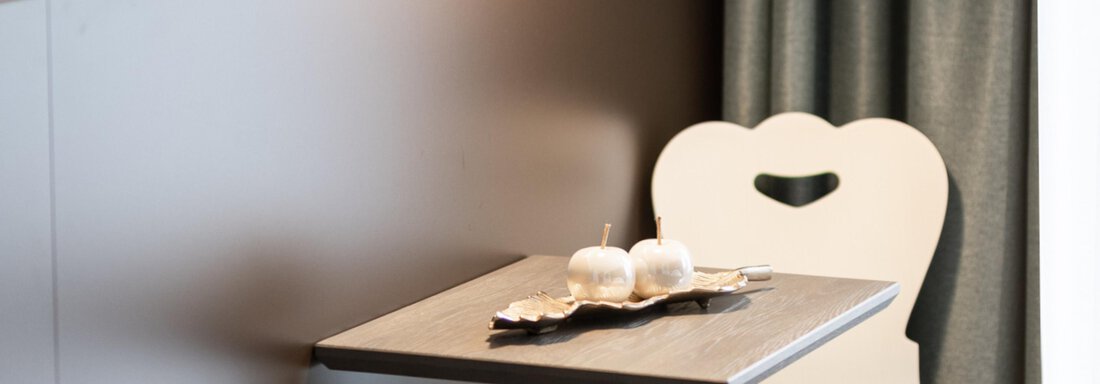 A cozy table with decorative objects stands next to a chair with a heart-shaped backrest. The room has a modern and inviting character. - Haus Verwall Appartements - Obergurgl 