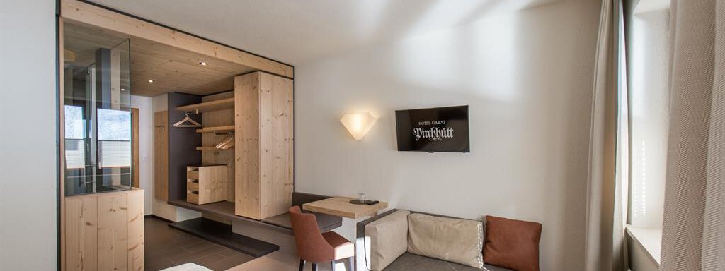 A modern room with a double bed, a cozy seating area, and a desk. The wooden paneling and the clean design create a pleasant atmosphere. - Hotel-Garni Pirchhütt - Obergurgl 