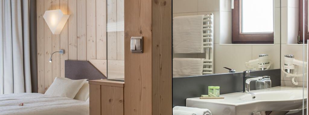 A modern room with wooden paneling and a comfortable bed is visible. On the other side, there is an elegant bathroom with a sink and towels. - Hotel-Garni Pirchhütt - Obergurgl 