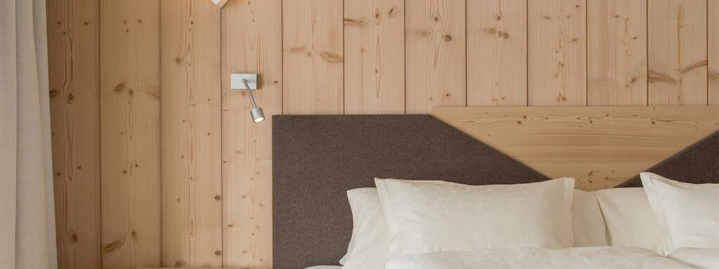 A modern bedroom with wooden walls and a comfortable bed. The simple lighting and decorative elements create a calm atmosphere. - Hotel-Garni Pirchhütt - Obergurgl 