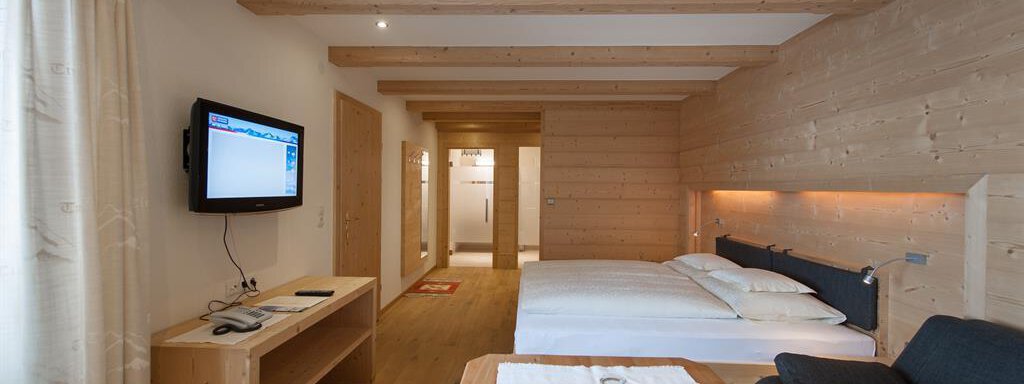 Familienzimmer A modern hotel room with wooden decor, two beds, and a television. There is also a small table and a cozy seating area. - Hotel-Garni Pirchhütt - Obergurgl