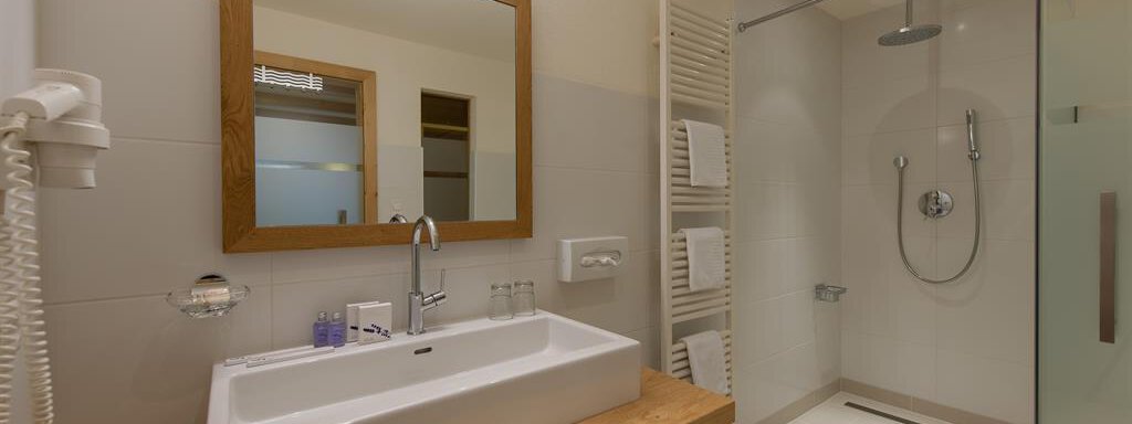 A modern bathroom with a large mirror and an elegant shower. The wooden shelves provide space for towels and personal care products. - Hotel-Garni Pirchhütt - Obergurgl 