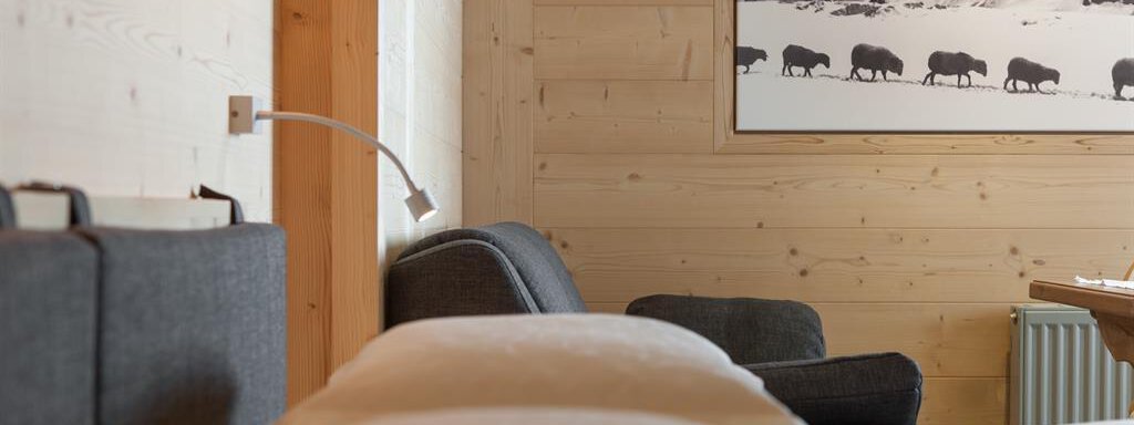A cozy interior with wooden paneling and modern furniture. On the wall hangs a picture of a mountain landscape with animals. - Hotel-Garni Pirchhütt - Obergurgl 