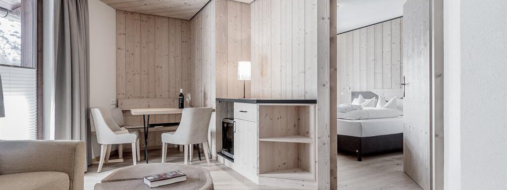 Familiensuite "Montanara" A modern living room with wooden walls and a cozy seating area. The room is bright and inviting, with a small dining area and another room in the background. - Hotel-Garni Pirchhütt - Obergurgl