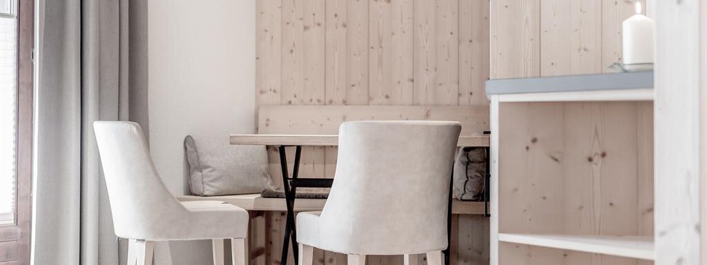 A bright room with two white chairs and a wooden table. The walls are paneled with natural wood, and there are large windows with curtains. - Hotel-Garni Pirchhütt - Obergurgl 