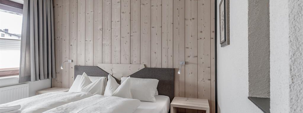 A cozy bedroom with a double bed and light wooden walls. There are two nightstands and curtains that gently filter the light. - Hotel-Garni Pirchhütt - Obergurgl 