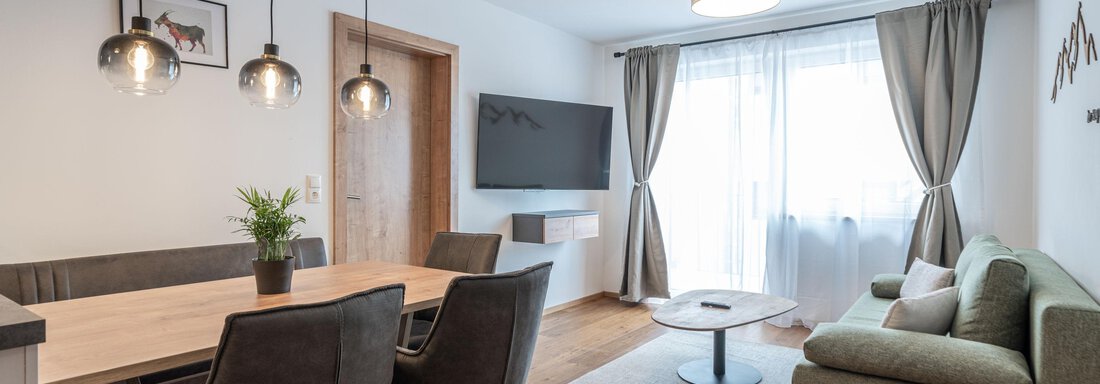A modern living room with a green sofa, a table, and chairs. Large windows let in a lot of light and the room feels inviting. - Mein Gaisberg - Obergurgl 