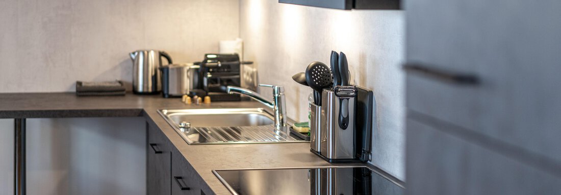 A modern kitchen with dark cabinets and a clear, tidy design. The countertop is well equipped with cooking utensils and appliances. - Mein Gaisberg - Obergurgl 