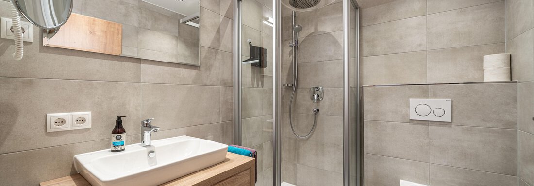 A modern bathroom with a shower and a wooden sink. The walls are painted in a neutral gray tone. - Mein Gaisberg - Obergurgl 