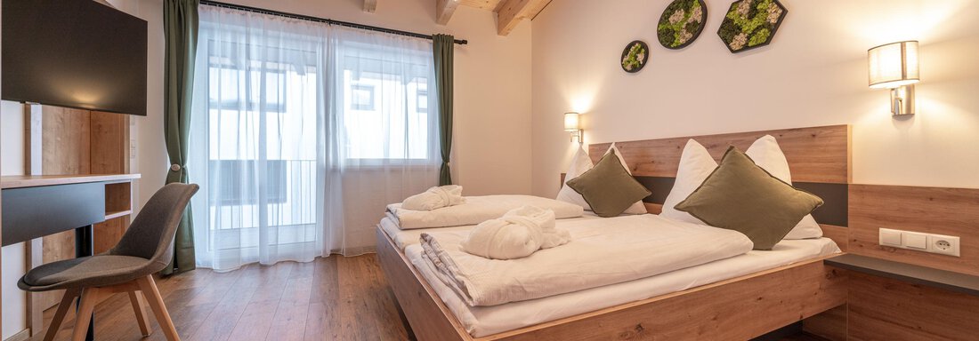 A modern bedroom with a large double bed and a television. The room features bright wooden elements and large windows that let in plenty of light. - Mein Gaisberg - Obergurgl 