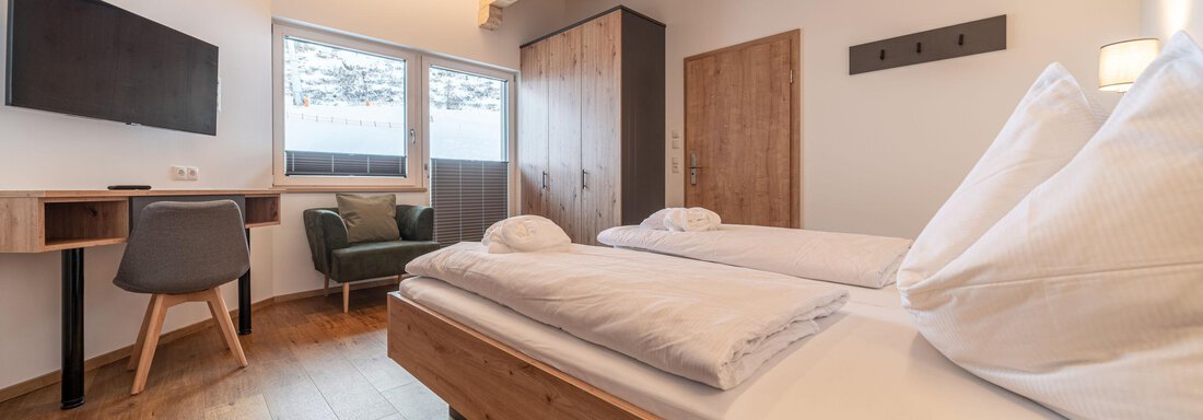 A cozy bedroom with wood decor and large windows. There are two beds and a small desk with a chair. - Mein Gaisberg - Obergurgl 