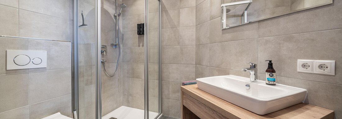 A modern bathroom with a glass shower and a sink on a wooden base. The walls are in neutral colors, providing a pleasant atmosphere. - Mein Gaisberg - Obergurgl 