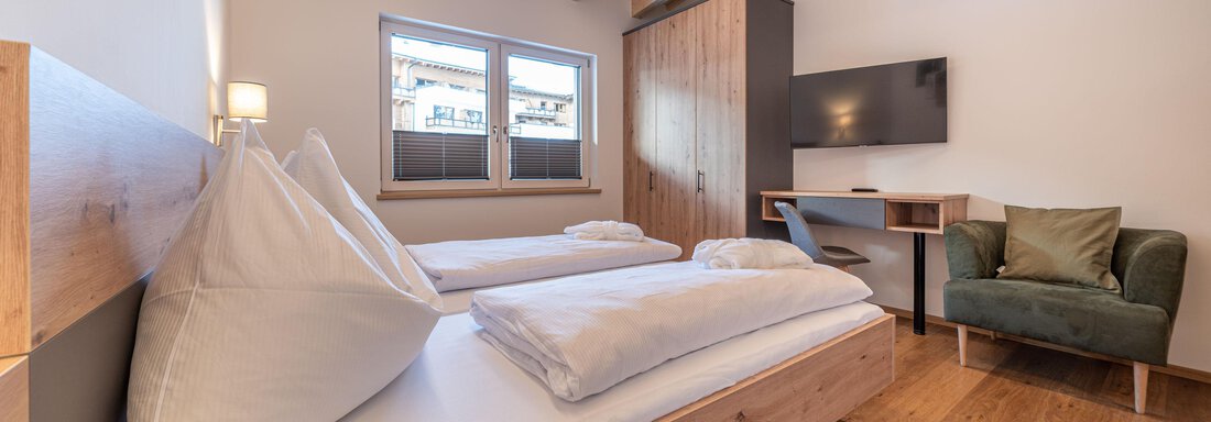 A cozy bedroom with two single beds and modern wood design. It features a television and a small seating area. - Mein Gaisberg - Obergurgl 