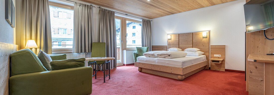 A cozy hotel room with wooden walls and carpeted floor. There is a large bed, atmospheric lighting, and a small table with chairs. - Schönblick Gurgl - Obergurgl 