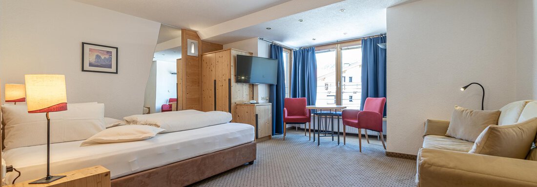 Doppelzimmer Typ B A modern hotel room with a large bed and a comfortable armchair. The room has large windows with a view of the city and is well-lit. - Schönblick Gurgl - Obergurgl