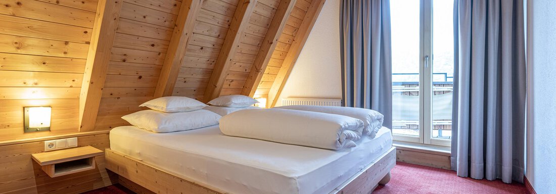 A cozy bedroom with a wooden bed and two pillows. Large windows let in plenty of light and offer a view outside. - Schönblick Gurgl - Obergurgl 