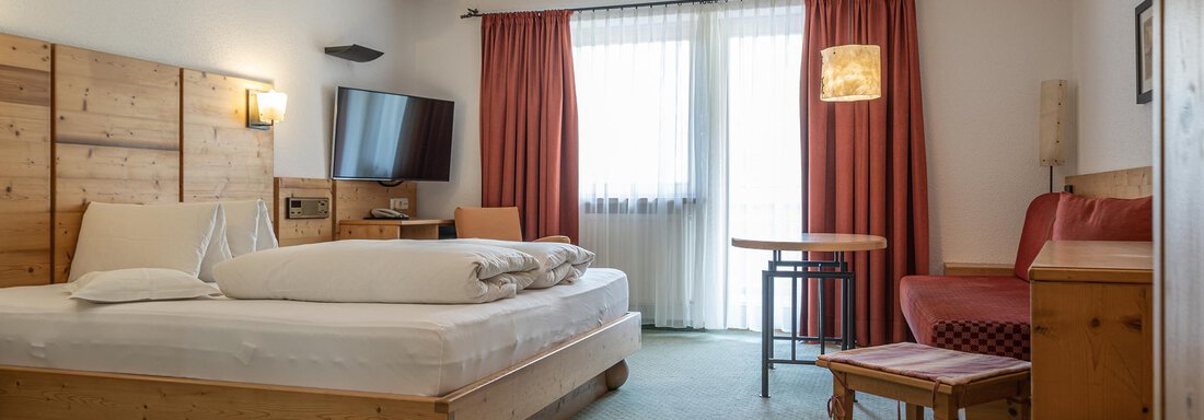 A cozy hotel room with a large bed, a table, and chairs.  
Large windows let in plenty of daylight. - Schönblick Gurgl - Obergurgl 