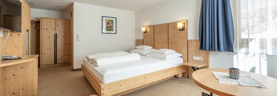 A modern room with a large bed and a cozy red sofa. There are windows with curtains and a small table. - Schönblick Gurgl - Obergurgl 