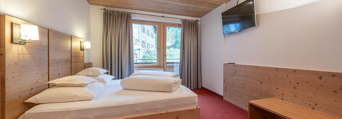 A cozy room with a large double bed and wooden details. The windows offer a view outside and the floor is covered with red carpet. - Schönblick Gurgl - Obergurgl 