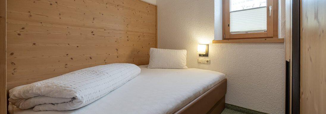 A simple bedroom with a single bed and warm wood paneling. The window lets in daylight and offers a view outside. - Schönblick Gurgl - Obergurgl 