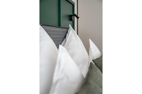 A cozy headboard with several pillows in different textures. The white pillows are clearly visible and the wall has a simple, modern design. - The Moss - Your unique hideaway - Obergurgl 