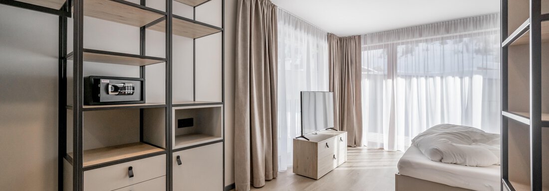 A modern bedroom with a large window and bright light. The furnishings are minimalist with a shelf and a television. - The Moss - Your unique hideaway - Obergurgl 
