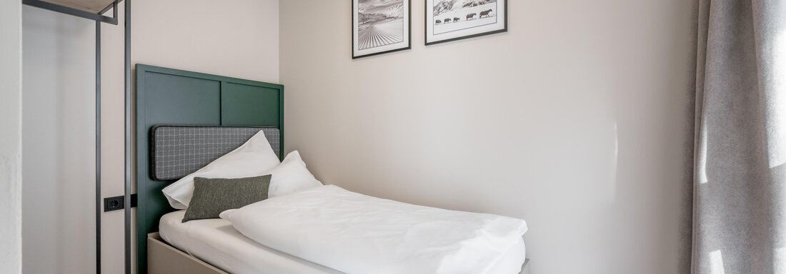 A simple, modern bedroom with a single bed and a minimalist design. On the wall, two pictures hang, and there is an open metal wardrobe. - The Moss - Your unique hideaway - Obergurgl 