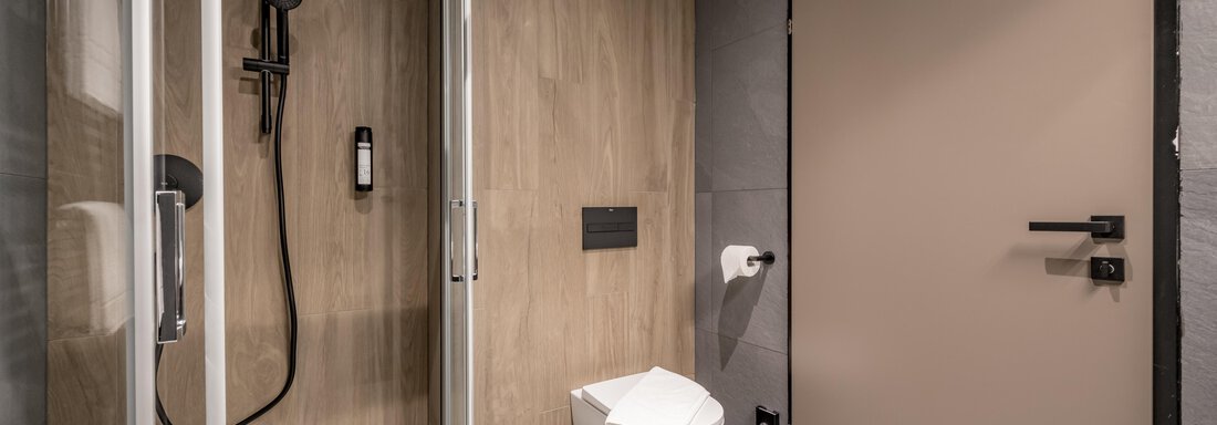 A modern bathroom with a shower and a toilet. The walls are predominantly designed in a wood look. - The Moss - Your unique hideaway - Obergurgl 