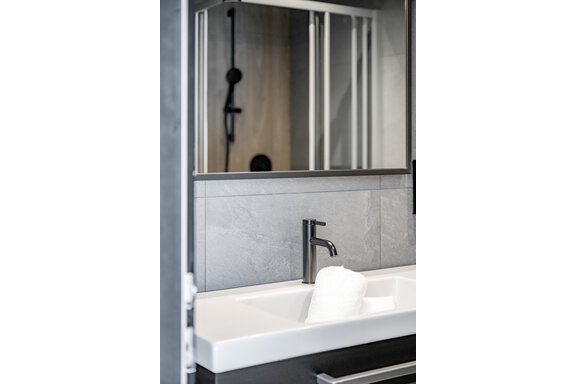A modern bathroom with a stylish sink and a black-style faucet. In the background, a shower with gray tiles and a mirror can be seen. - The Moss - Your unique hideaway - Obergurgl 