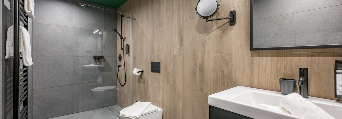 A modern bathroom with light tiles and wood paneling. It includes a shower, a toilet, and a sink with stylish fixtures. - The Moss - Your unique hideaway - Obergurgl 