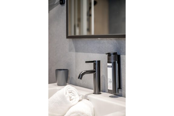 A modern bathroom with a black faucet and a soap dispenser. Clean, folded towels are next to a sink. - The Moss - Your unique hideaway - Obergurgl 