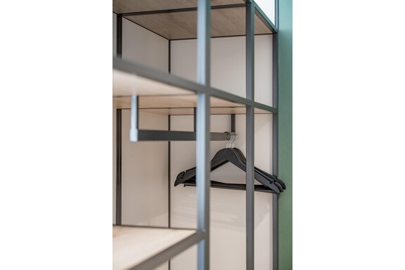 A modern wardrobe with open shelves and a clothes hanger. The structure consists of a black frame and light wood panels. - The Moss - Your unique hideaway - Obergurgl 