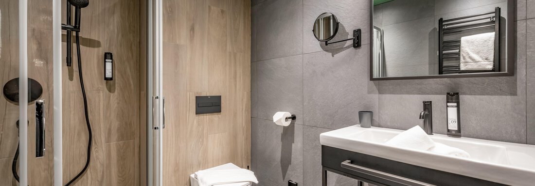 A modern bathroom with a shower, a toilet, and an elegant sink. The walls are in various shades of gray, complemented by wooden details. - The Moss - Your unique hideaway - Obergurgl 