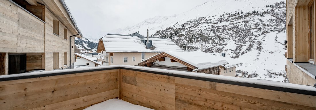 A balcony with wooden cladding and fresh snow. In the background, snow-covered mountains and alpine houses are visible. - The Moss - Your unique hideaway - Obergurgl 