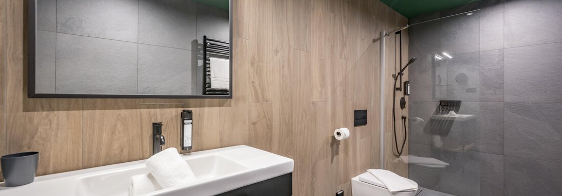A modern bathroom with light wood and grey tiles. There is a shower, a sink, and a large mirror. - The Moss - Your unique hideaway - Obergurgl 