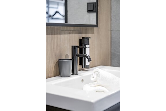 A modern bathroom with a stylish sink and a black faucet. Next to the sink are a clean towel and a gray cup. - The Moss - Your unique hideaway - Obergurgl 