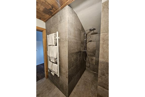 Dusche in einem modern gestalteten Badezimmer mit grauen Fliesen. Handtücher werden ordentlich auf einem Handtuchhalter aufbewahrt. - Almhof Mareil - Ochsengarten