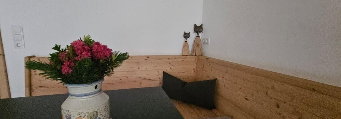 Ein gemütlicher Raum mit Holzverkleidung und einer dunklen Tischfläche. In der Mitte steht eine blühende Vase mit bunten Blumen. - Almhof Mareil - Ochsengarten