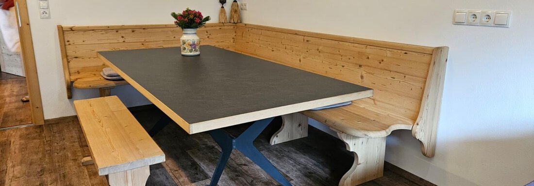Ein gemütlicher Essbereich mit einer Holzbank und einem modernen Tisch. Auf dem Tisch steht eine Blumenvase, die den Raum freundlich gestaltet. - Almhof Mareil - Ochsengarten
