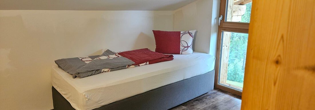 Ein gemütliches Zimmer mit einem Einzelbett und großen Fenstern. Die Wände sind schlicht und der Boden hat einen Holzlook. - Almhof Mareil - Ochsengarten