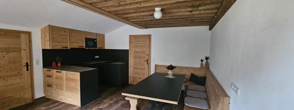 Wohnküche Karl A modern room with wooden paneling and an open loft gallery. The space features a kitchenette, a dining table, and a cozy seating area. - Almhof Mareil - Ochsengarten